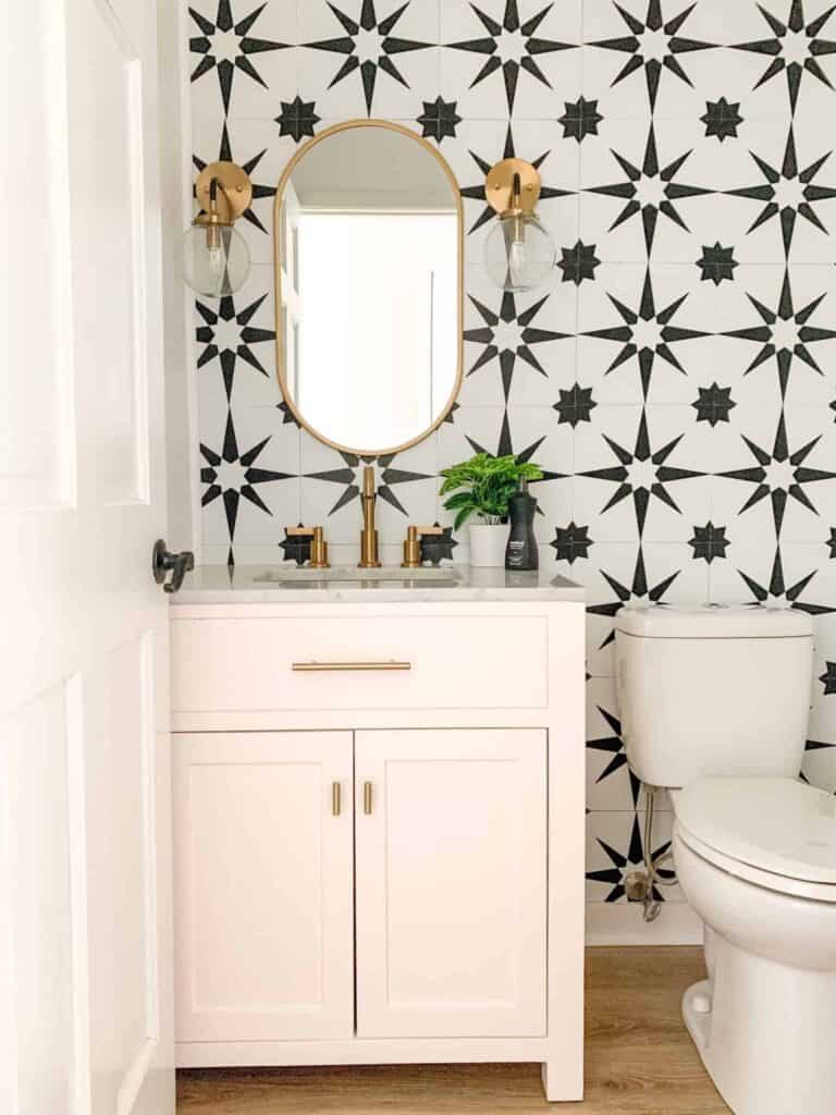 Pink powdered bathroom with geometric black and white tile backsplash and gold accents.