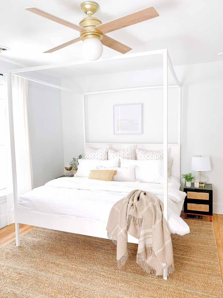 White bedroom with a DIY king canopy bed and rattan rug.