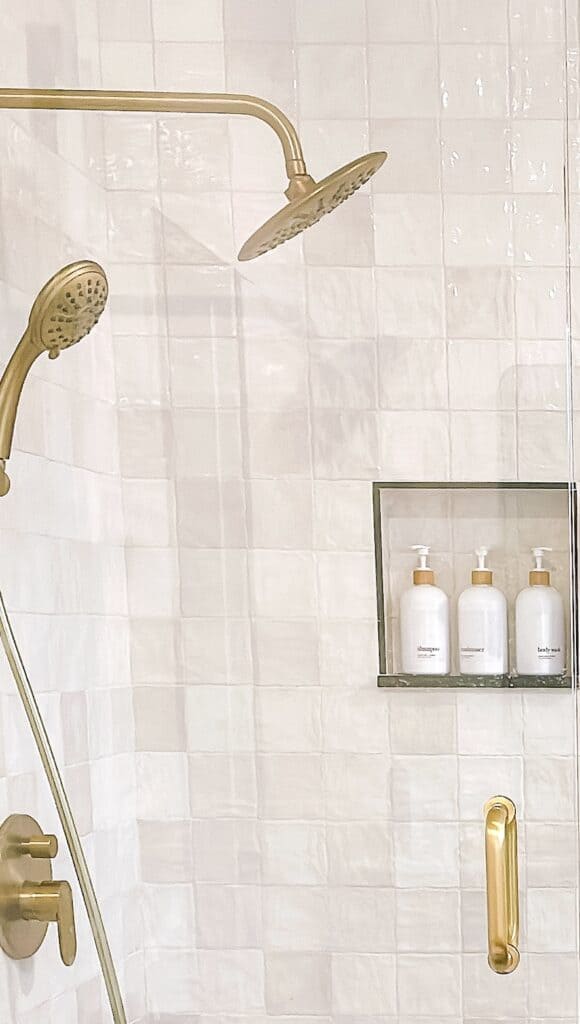 Shower close up of square tiles with natural stones and gold hardware.