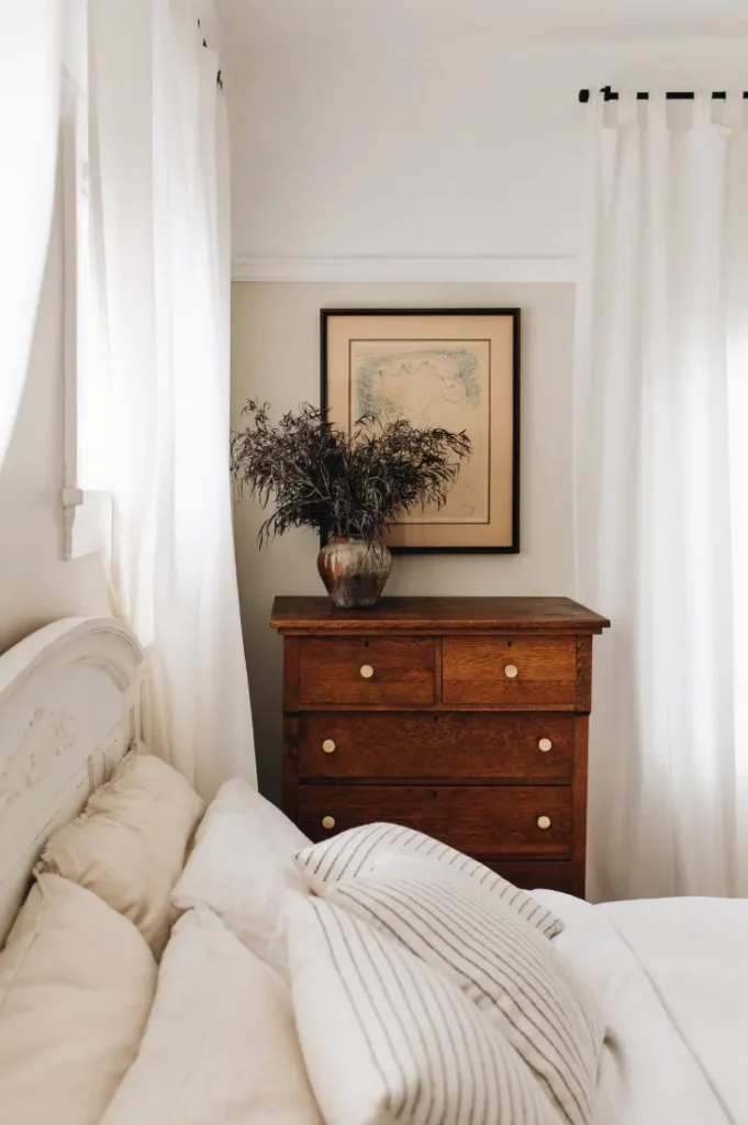 Dark wooden antique dresser with white bed and bedding.