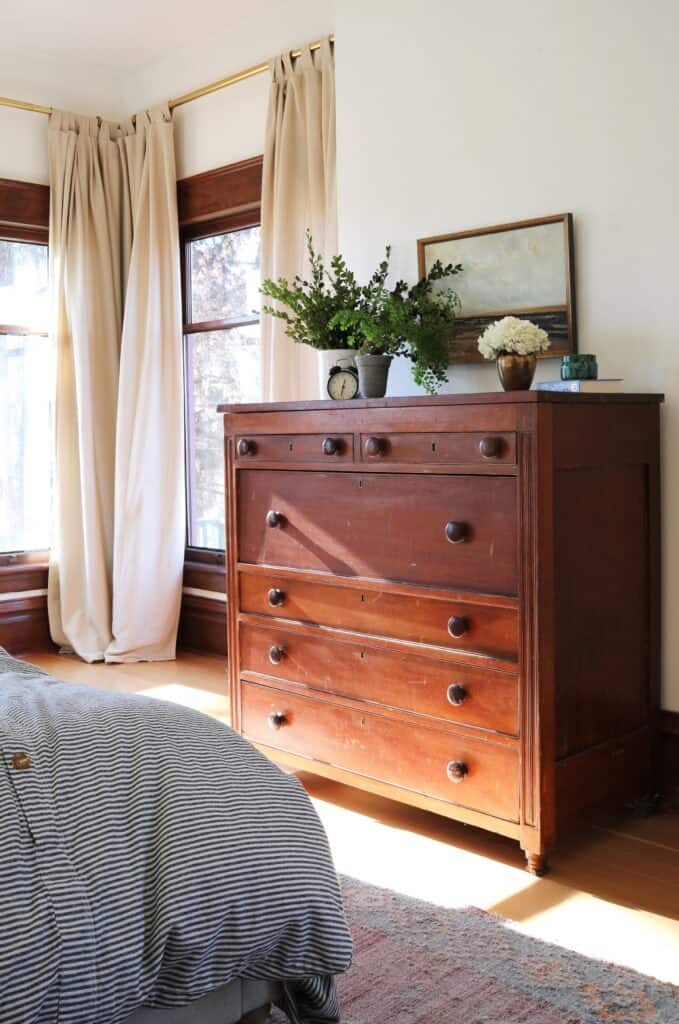 Large wooden chest of drawers with vase of flowers.