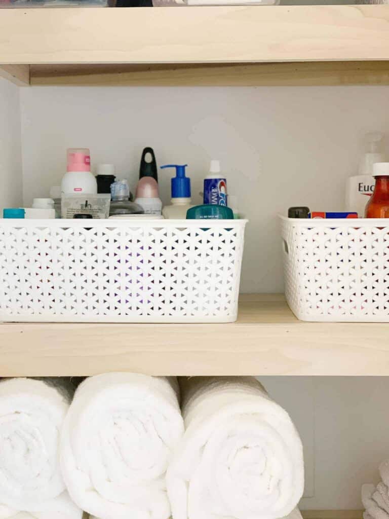 Bathroom cabinets with rolled towels and white baskets.