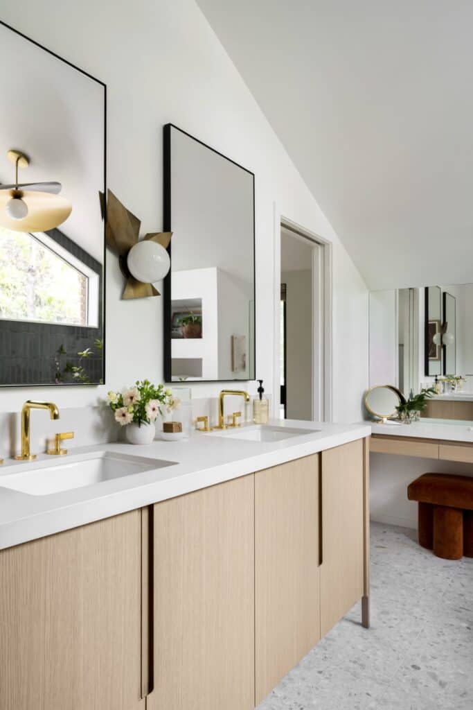 Master bathroom with modern elements of natural wooden tones, double sink, gold faucets, and black rectangular mirrors.