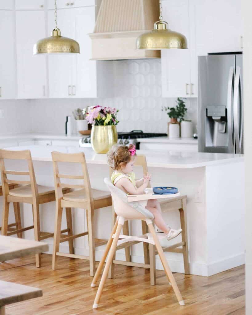 Baby sitting in a high chair in front of a white kitchen.