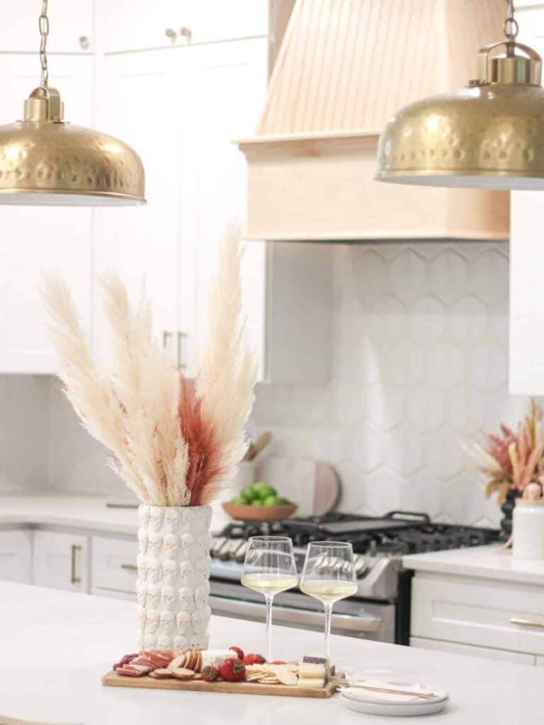 White kitchen with a charcuterie board, two glasses of wine, and a DIY skeleton vase filled with wheat grass.