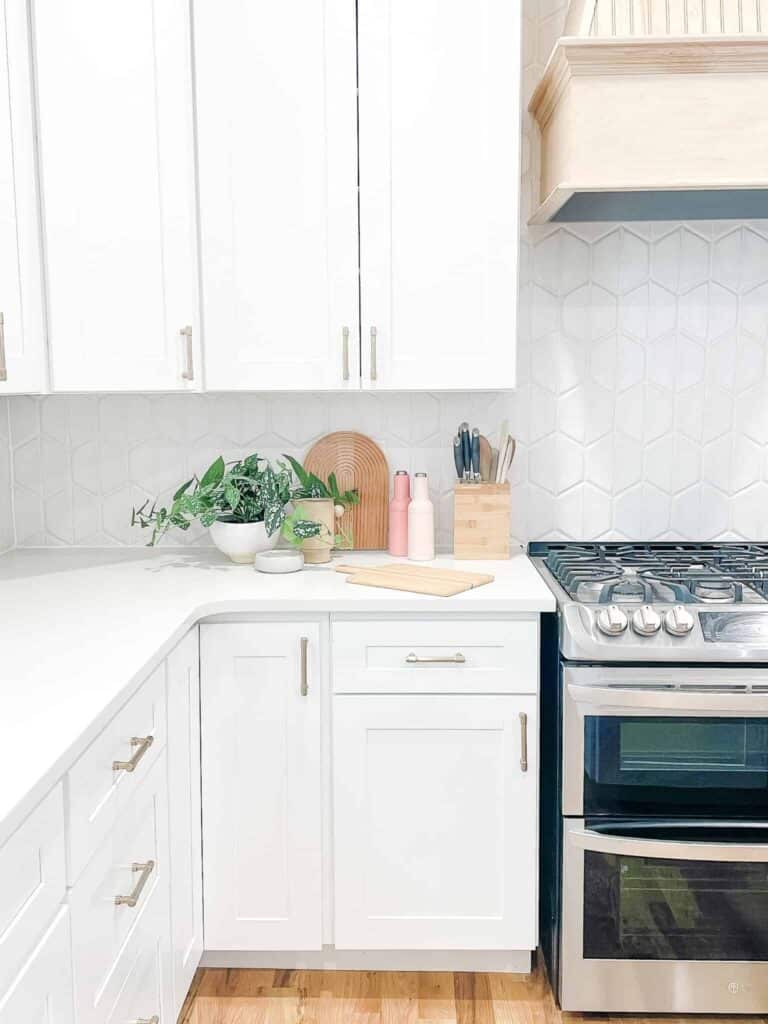 Close up of kitchen cabinet corner with stove, hood, and cutting board.