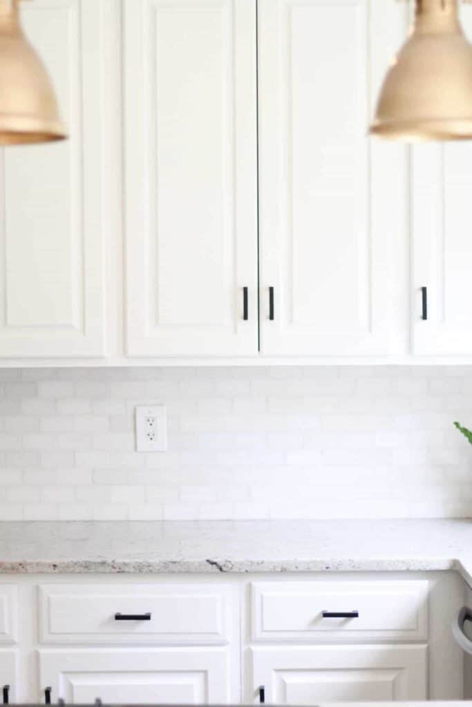 White cabinets in an all white kitchen with black hardware and brass lighitng.