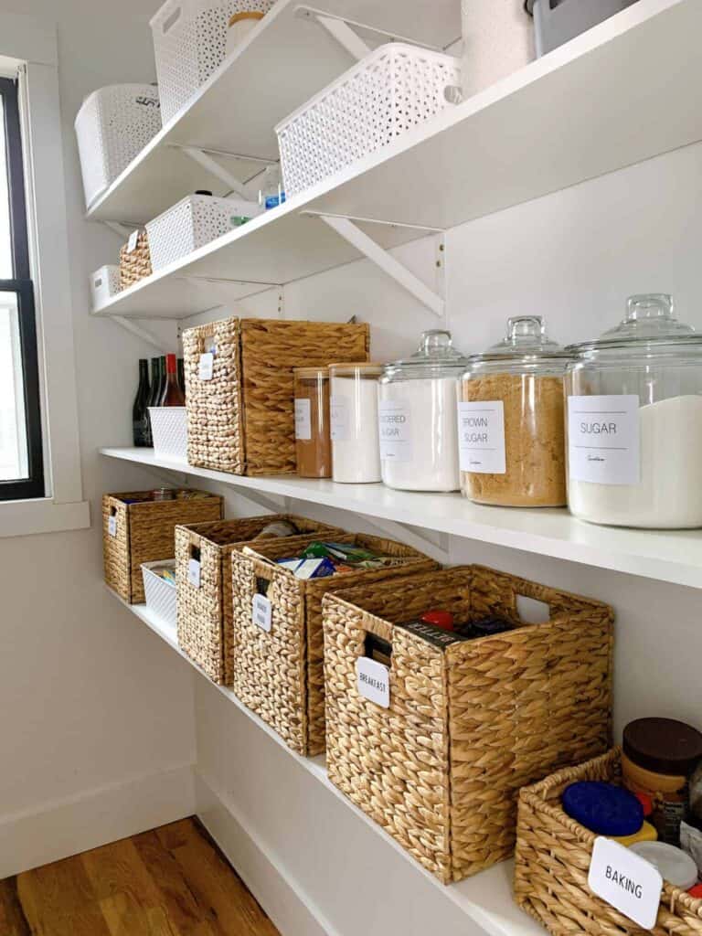 Inside a pantry with wicker baskets and glass jars labeled with essential foods.