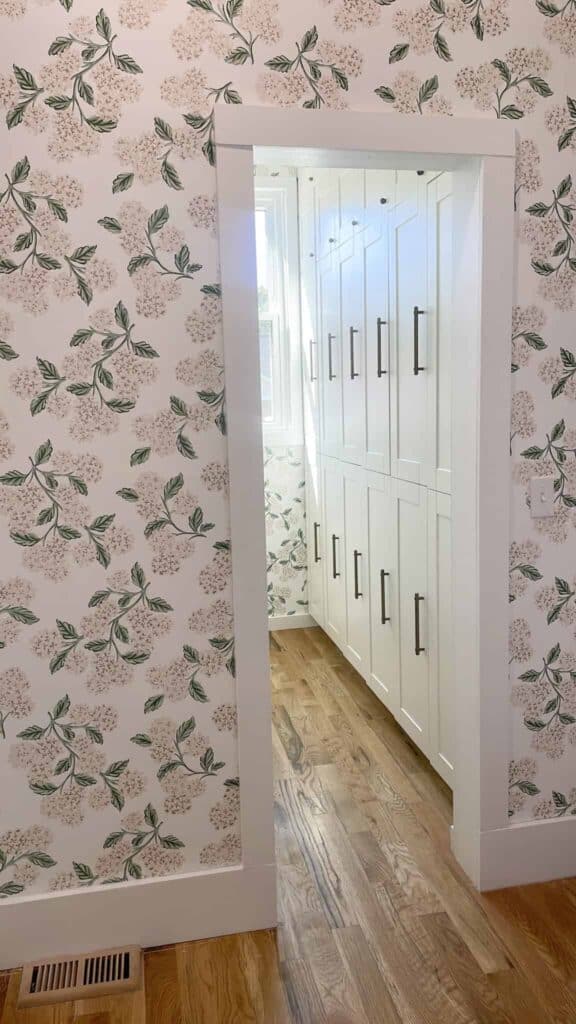 Butlers pantry with white cabinets and floral pink and white wallpaper.