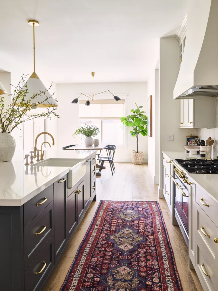 Homey kitchen with blue and deep red rug, dark cabinet island, and white brass cabinets and hardware.