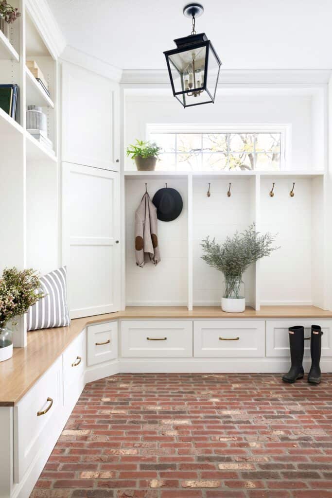 An all white mudroom with natural wood and red brick flooring.