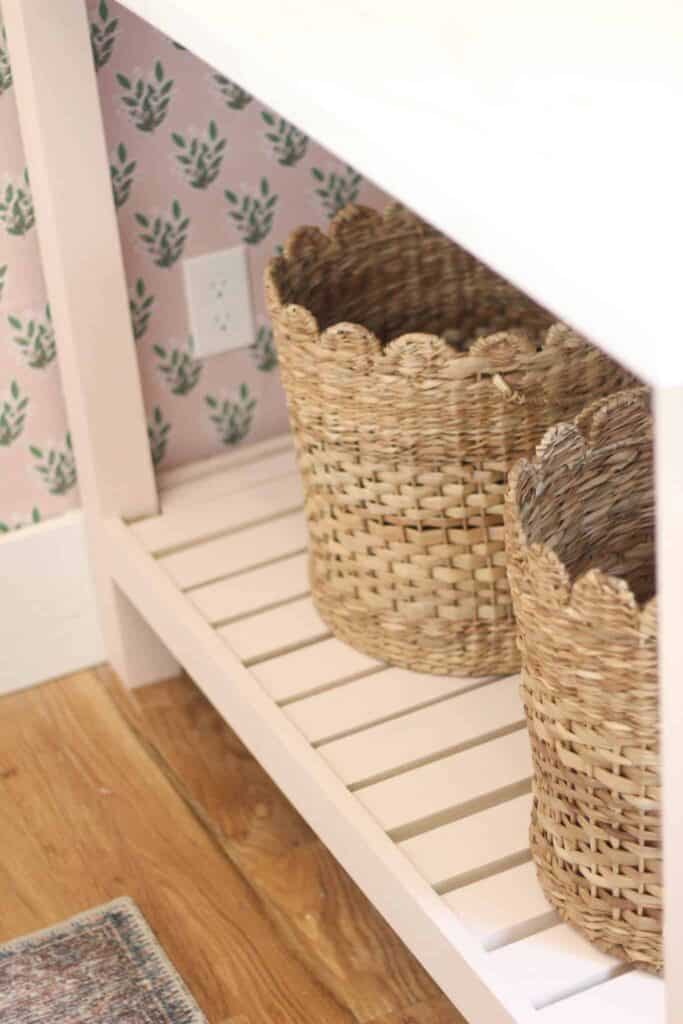 Wicker baskets under a DIY table with pink and green floral wallpaper in the background.