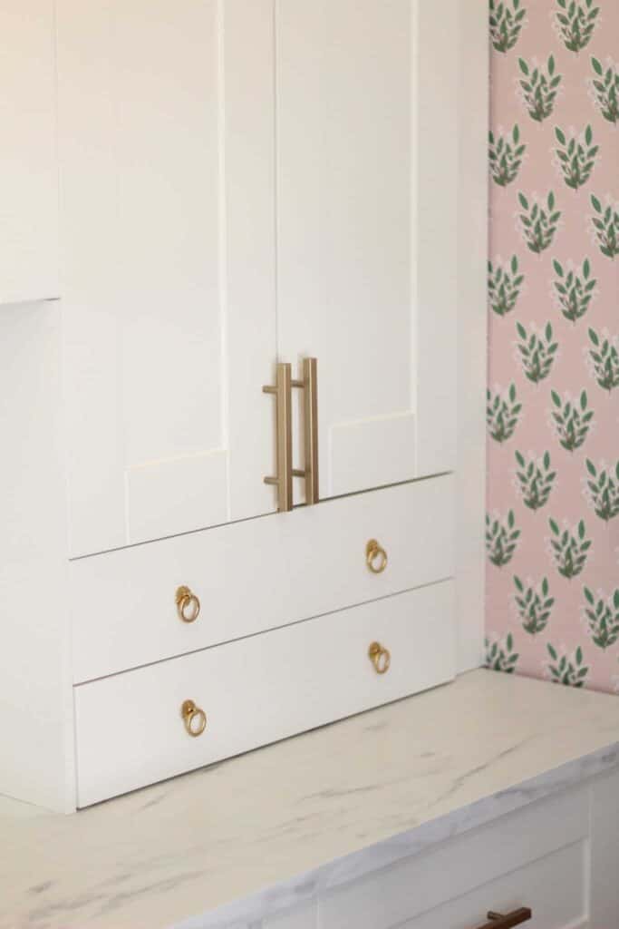 Close up of a white office cabinet and green and pink floral wallpaper.