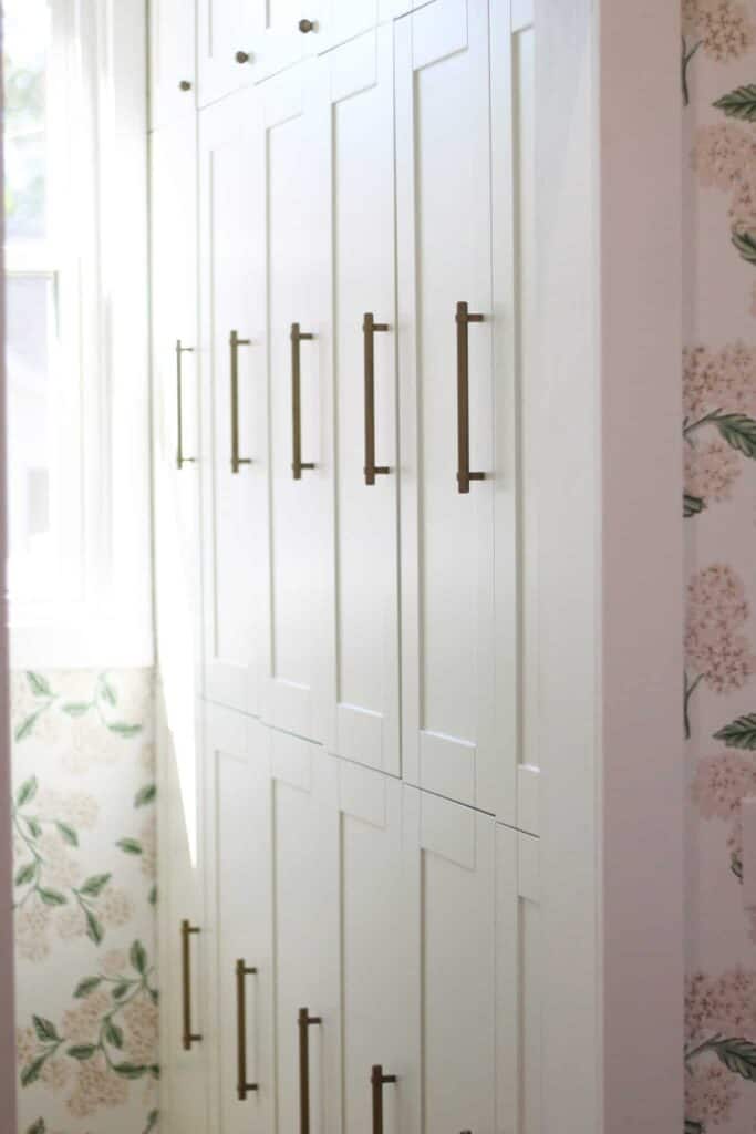 Close up of a pantry white cabinet and floral pink and green wallpaper.