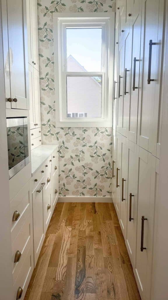 Butler pantry with floral wallpaper and floor to ceiling white cabinets.