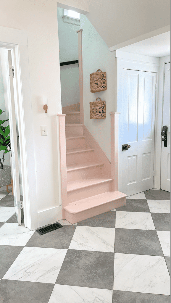 Mudroom grey and white tile marble floors with a pink staircase leading upstairs and wicker baskets hanging on the walls.