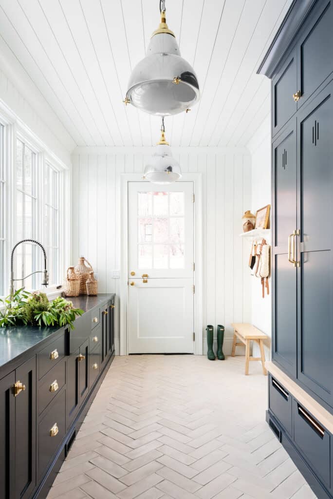 Natural stone herringbone tile offsets the dark cabinetry and dark countertops in this mudroom.