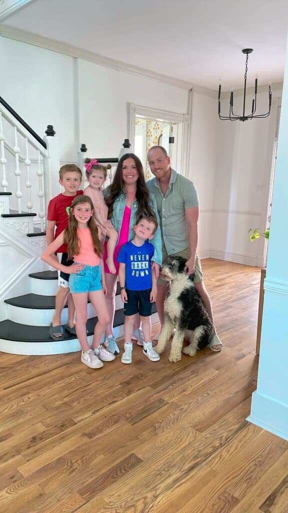 Family of 6 smiling in a house with a dog.