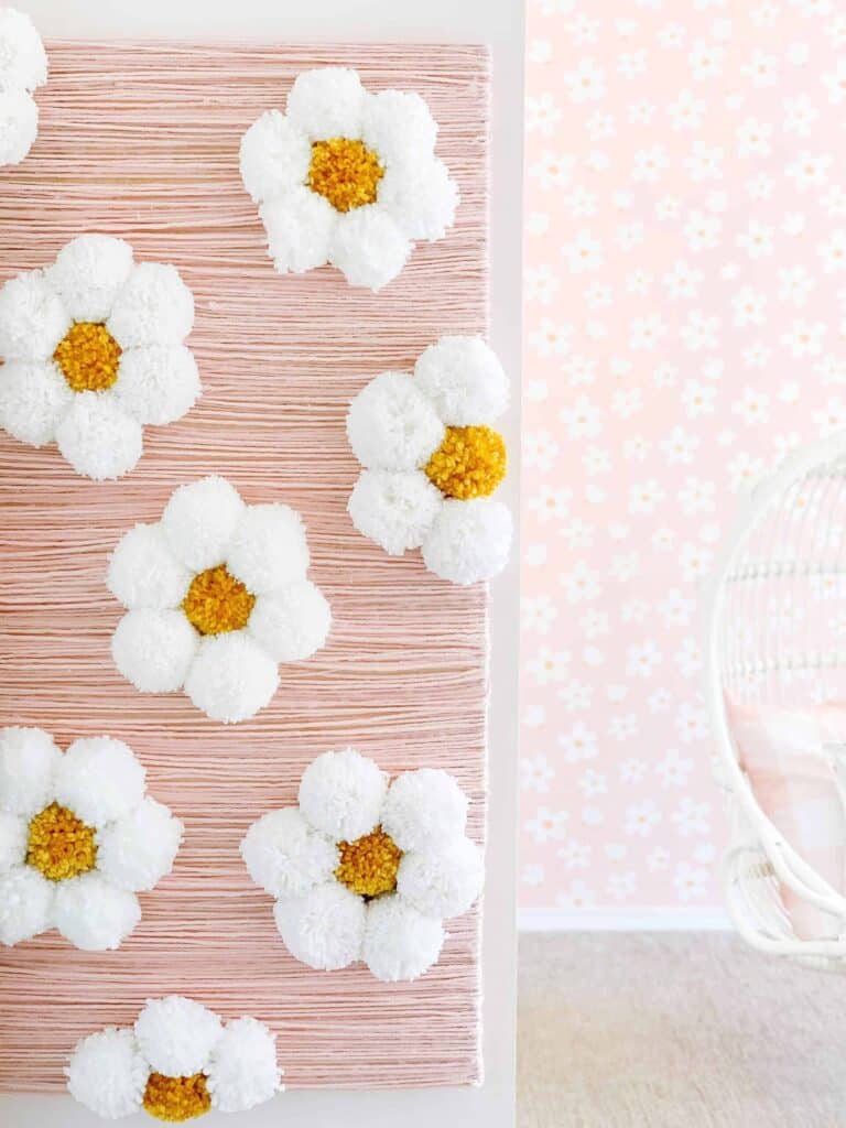 Make your own statement wall like this DIY Daisy Wall made from yarn and pom poms for a toddler girl bedroom on a budget.