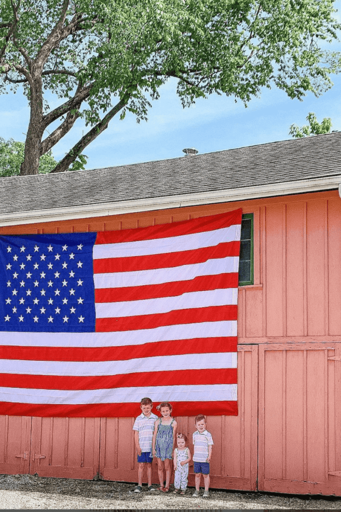 Barn with large American flag on it with kids in front of flag.