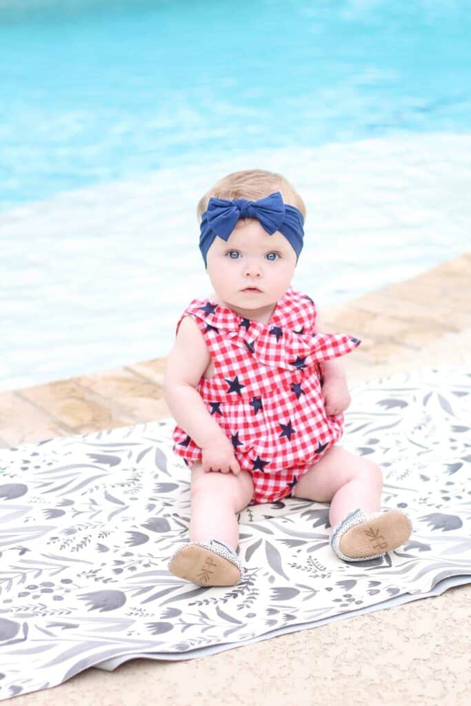 Baby girl in 4th of july outfit sitting by a pool.