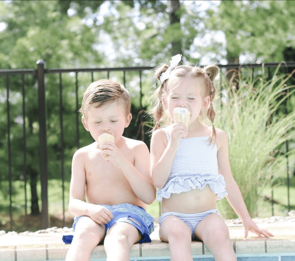 Little girl and little boy eating ice cream sitting by the pool.