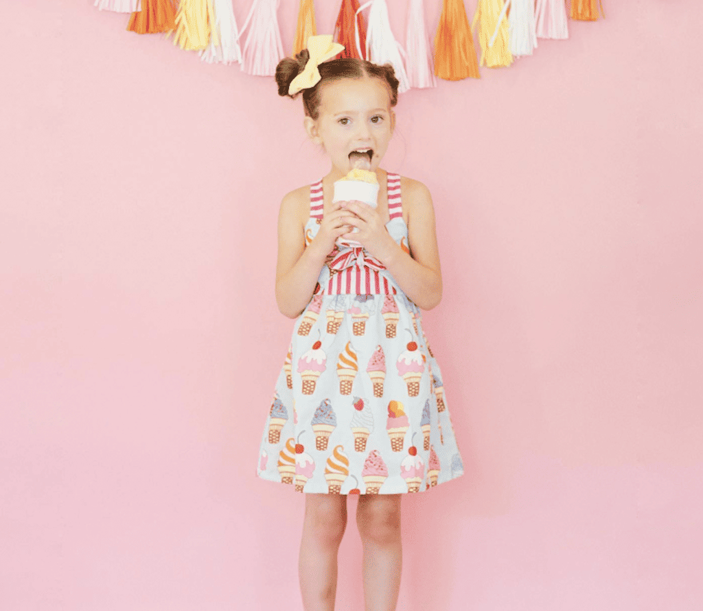 Little girl in ice cream dress eating an ice cream cone.