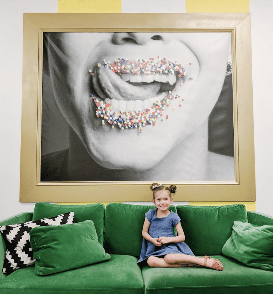 Little girl sitting on a green velvet couch with a sprinkles picture behind her.