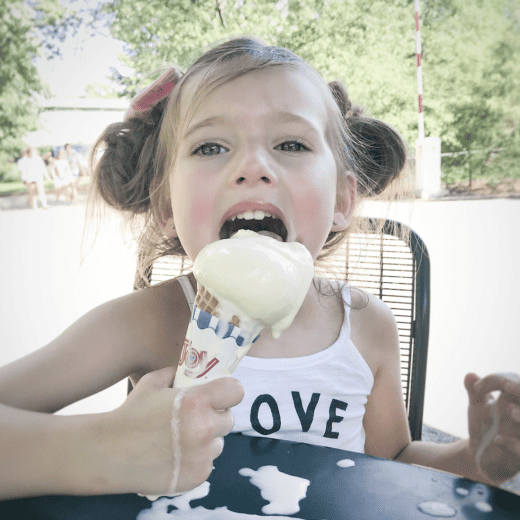 Little girl licking ice cream cone that is melting.