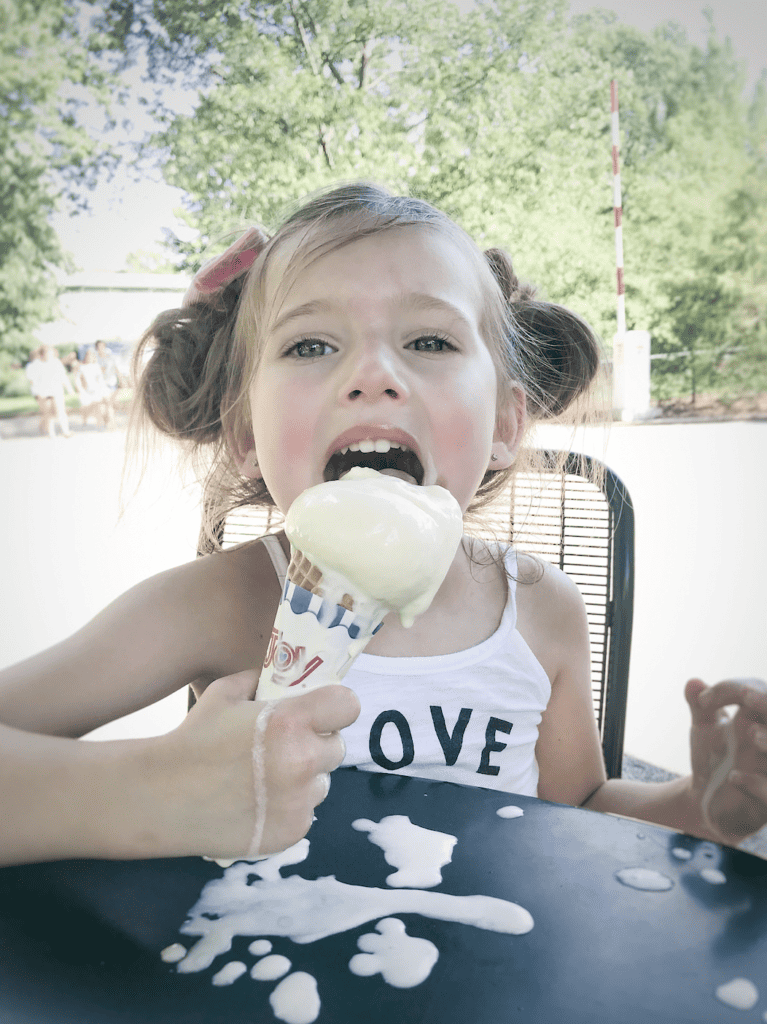 Little girl licking ice cream cone that is melting.
