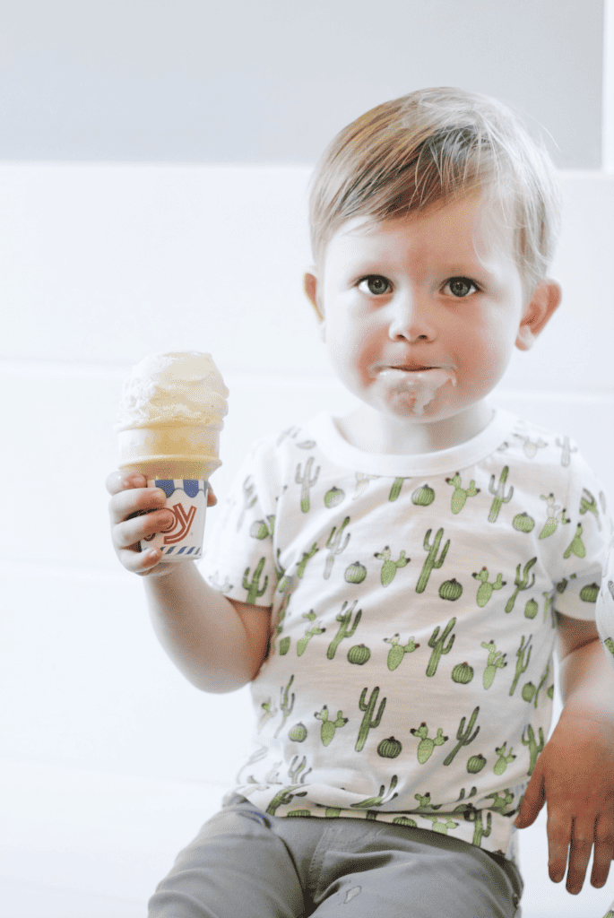 Toddler boy with ice cream on his face holding ice cream cone.