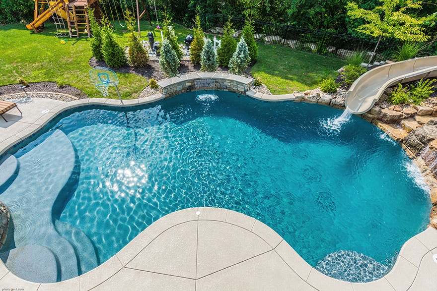 Luxury backyard pools with slides are  seen next to lots of green grass in this freeform pool.