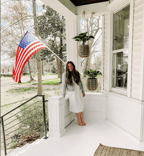 Woman standing on white porch with American Flag hanging