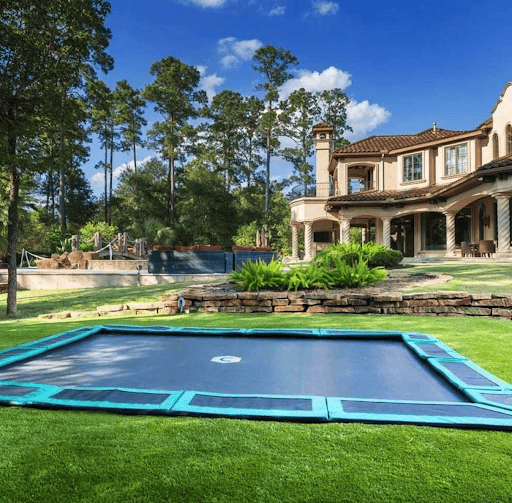 A backyard trampoline is seen in this backyard that is beautifully landscaped.