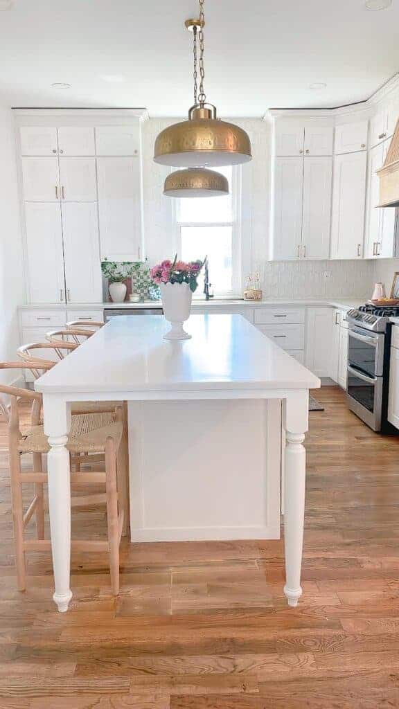 White kitchen island, brass kitchen pendant lights hanging over white island.