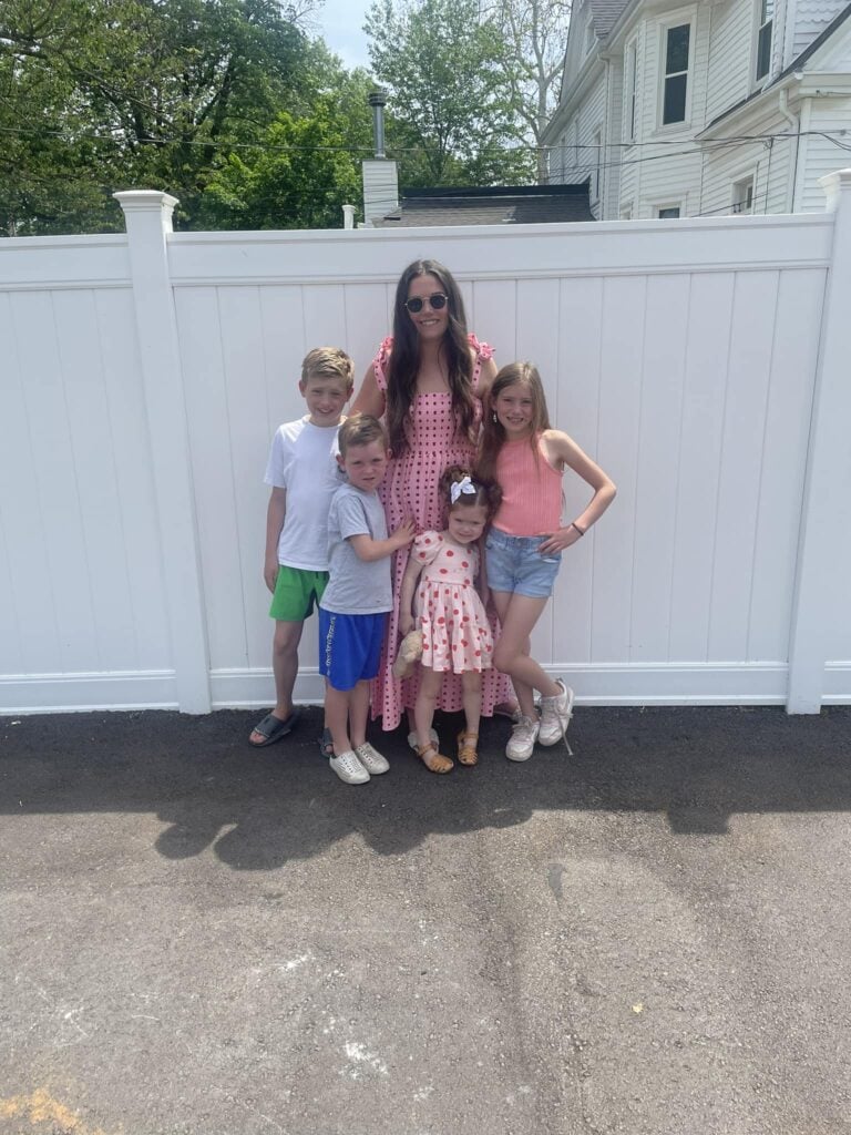 Mom with her four kids in front of white fence.