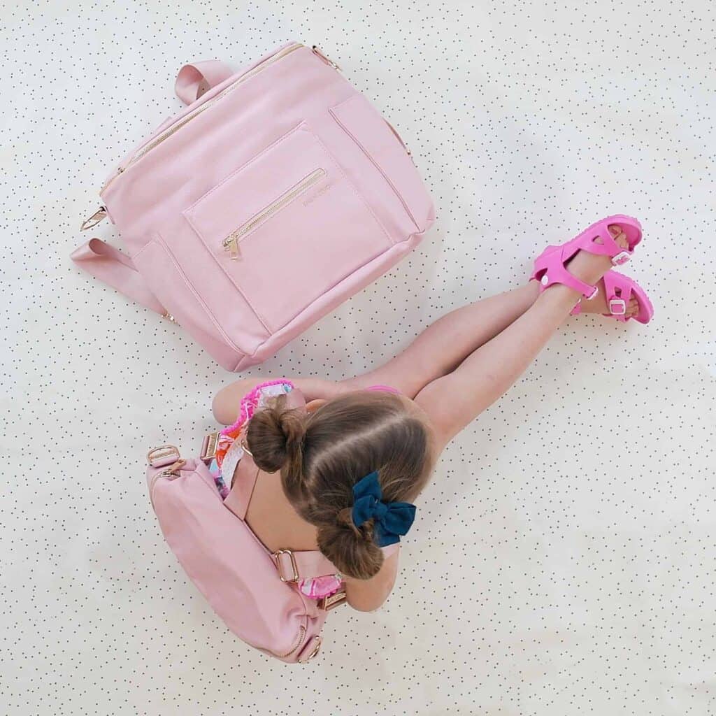 Best bags for moms can range in style. This little girl is posed next to a bag in pink.
