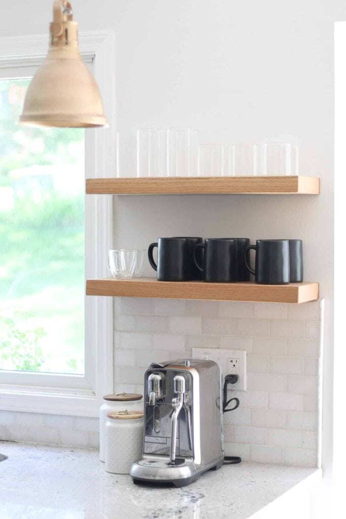Coffee station and open shelves with champagne pendant kitchen lights hanging over island.