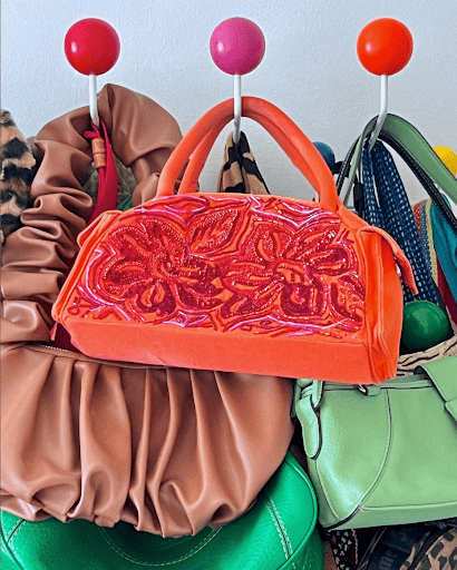 Bright color purses hang in a closet on a rack